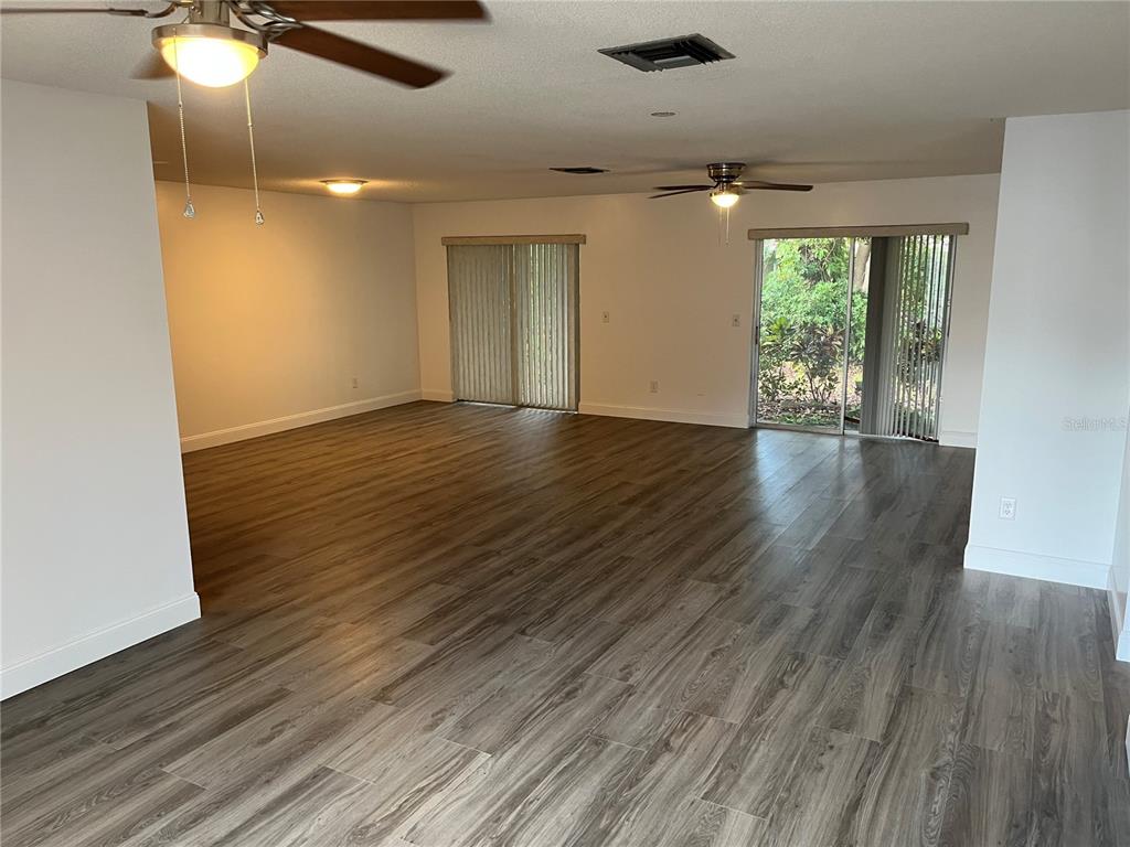 An open-concept living area features wood-look flooring, two ceiling fans, and sliding glass patio doors — 10108 BLUFF COURT, ORLANDO, FL