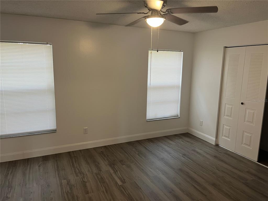 An empty bedroom features light-colored walls, wood-look flooring, two windows with blinds, and a closet — 10108 BLUFF COURT, ORLANDO, FL