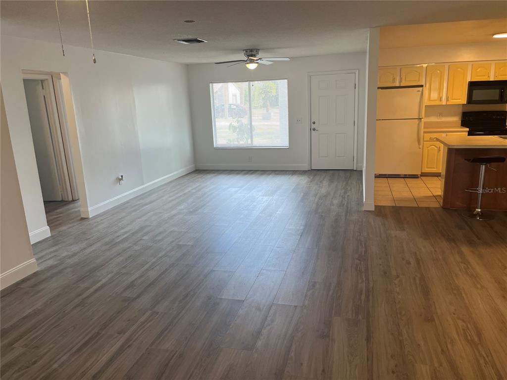 An open-concept living area features gray wood-look flooring, a ceiling fan, and an adjacent kitchen — 10108 BLUFF COURT, ORLANDO, FL