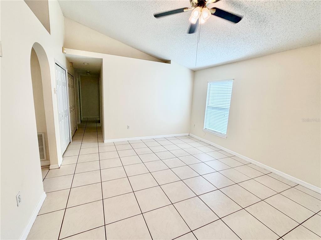 An empty room features white tile flooring, a vaulted ceiling with a fan, and a window — 13087 ODYSSEY LAKE WAY, ORLANDO, FL