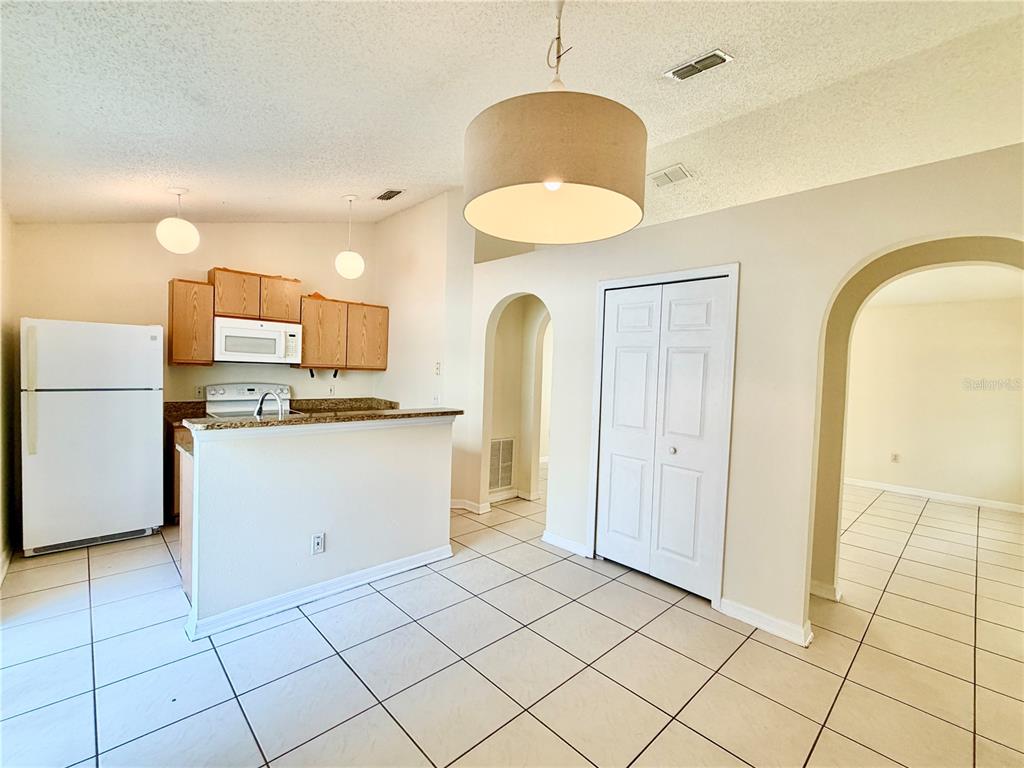 A kitchen with white appliances and light wood cabinets opens to a tiled dining area — 13087 ODYSSEY LAKE WAY, ORLANDO, FL