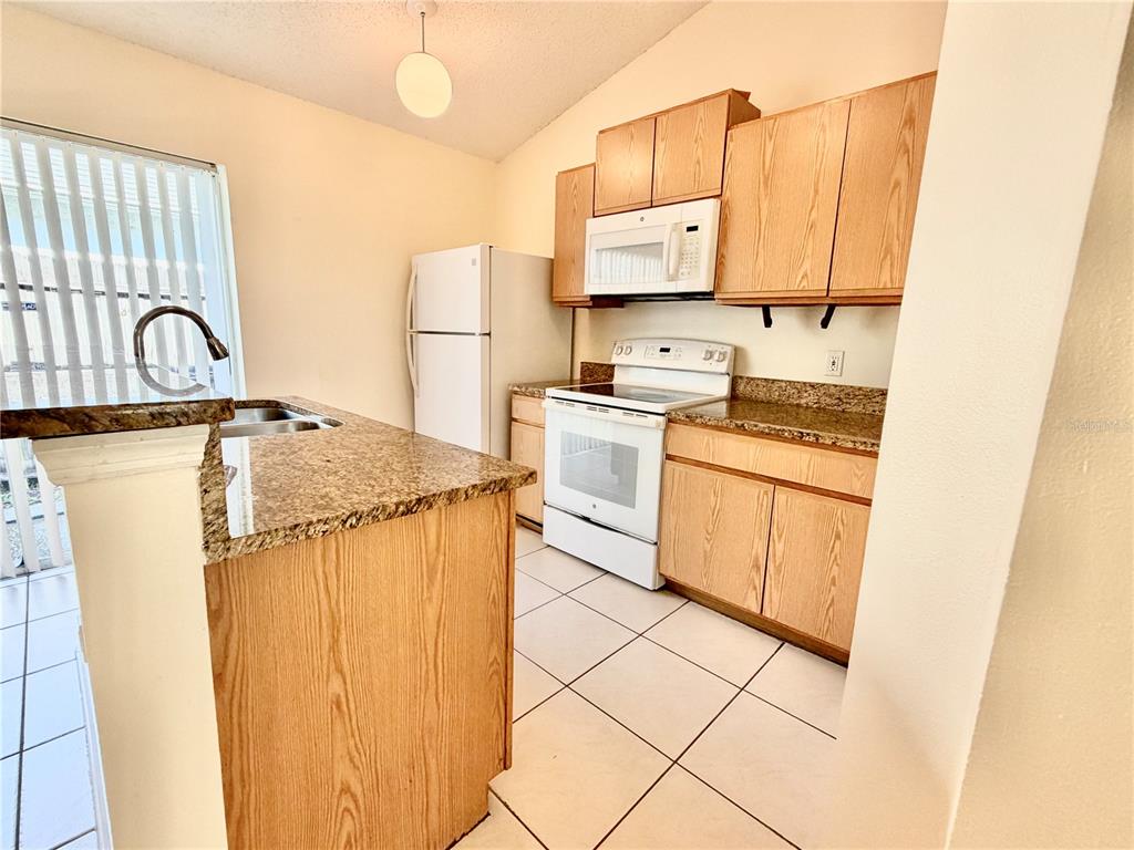 A kitchen features light wood cabinets, granite countertops, white appliances, and white tile flooring — 13087 ODYSSEY LAKE WAY, ORLANDO, FL