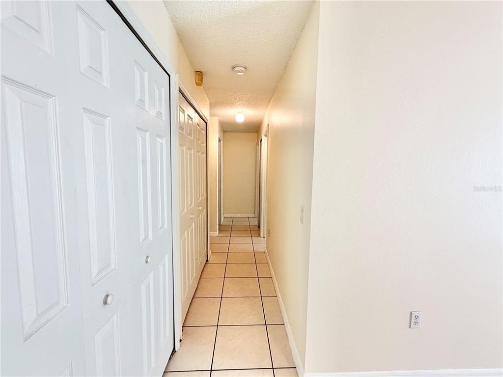 A hallway with white walls, tiled flooring, and multiple sets of white bifold closet doors — 13087 ODYSSEY LAKE WAY, ORLANDO, FL