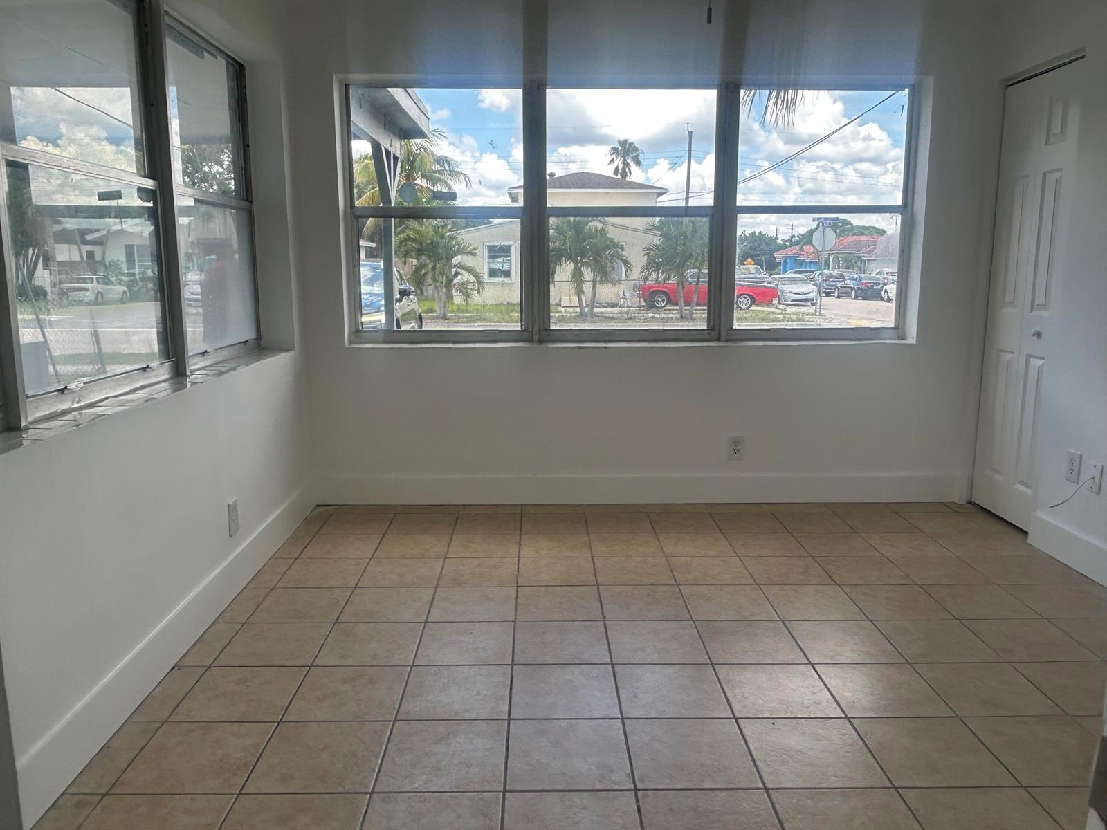 An empty room with beige tile flooring, white walls, and large windows overlooking a street — 1528 S Avenue # 0, Riviera Beach FL 33404, RIVIERA BEACH, FL