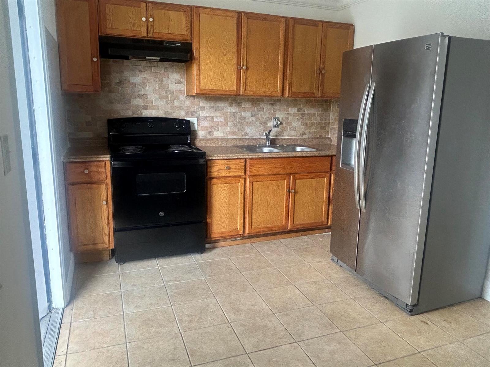 A kitchen features oak cabinets, a black stove, a stainless steel refrigerator, and tiled flooring — 1528 S Avenue # 0, Riviera Beach FL 33404, RIVIERA BEACH, FL
