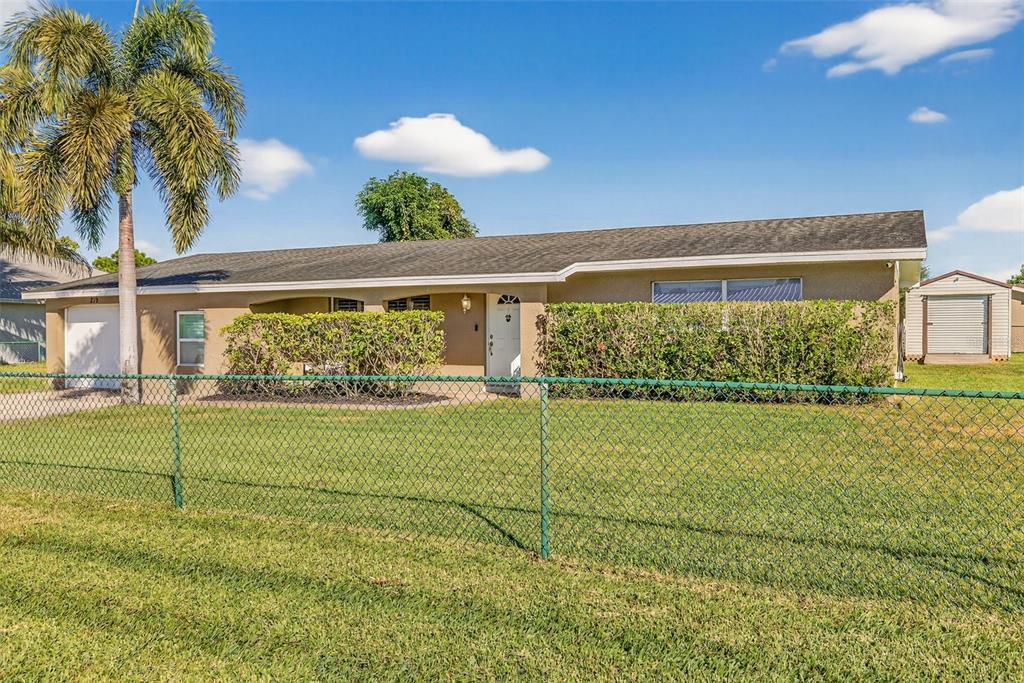 A single-story house with a palm tree, a chain-link fence, and a detached shed — 219 RICHMOND AVENUE S, LEHIGH ACRES, FL