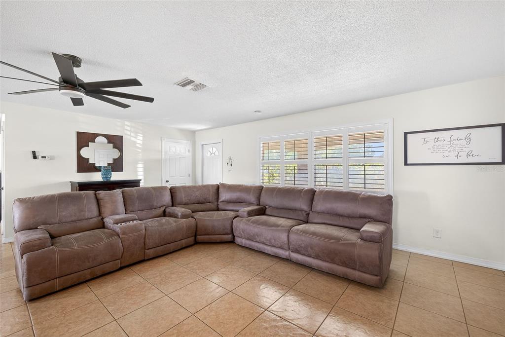 A living room features a large brown sectional sofa, tile flooring, and a ceiling fan — 219 RICHMOND AVENUE S, LEHIGH ACRES, FL