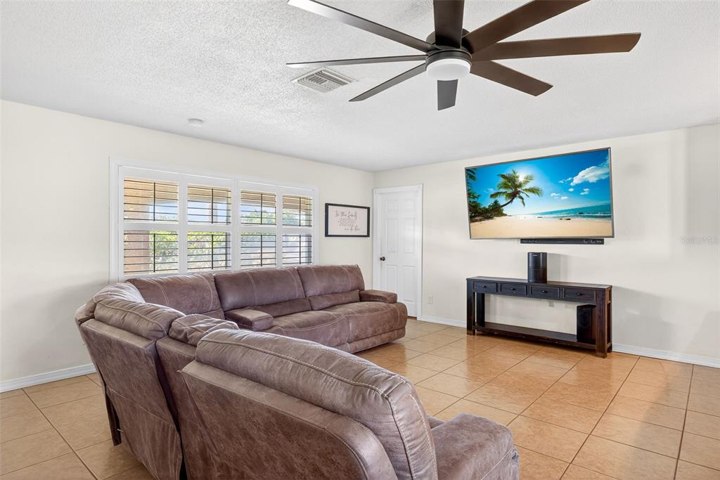A living room features a brown sectional sofa, a wall-mounted television, and tile flooring — 219 RICHMOND AVENUE S, LEHIGH ACRES, FL