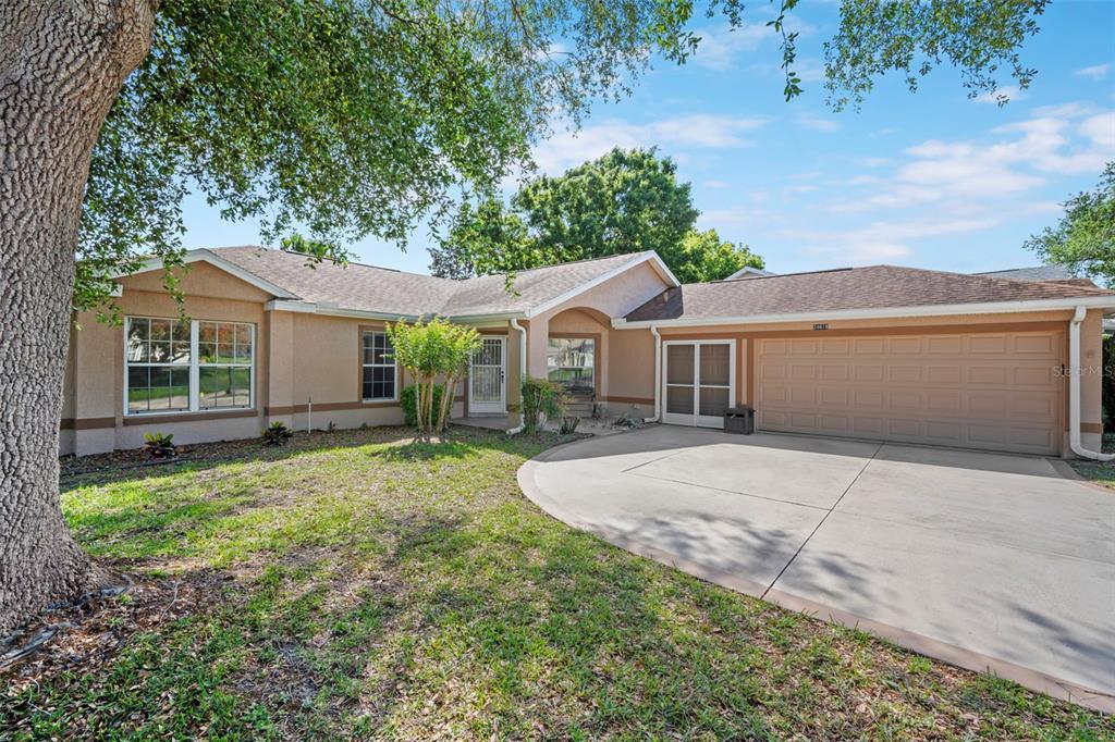 A single-story house with a tan stucco exterior, a two-car garage, and a concrete driveway — 24618 STILLRIDGE COURT, LEESBURG, FL