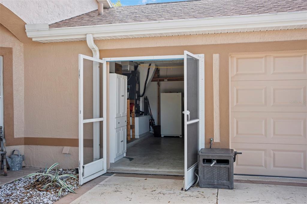 An open screen door reveals a garage interior with a white cabinet and utility equipment — 24618 STILLRIDGE COURT, LEESBURG, FL