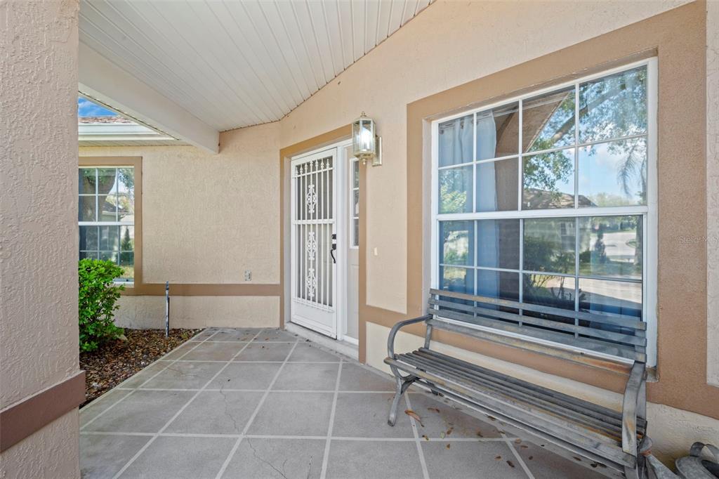 A covered concrete porch features a metal bench, a security screen door, and two windows — 24618 STILLRIDGE COURT, LEESBURG, FL