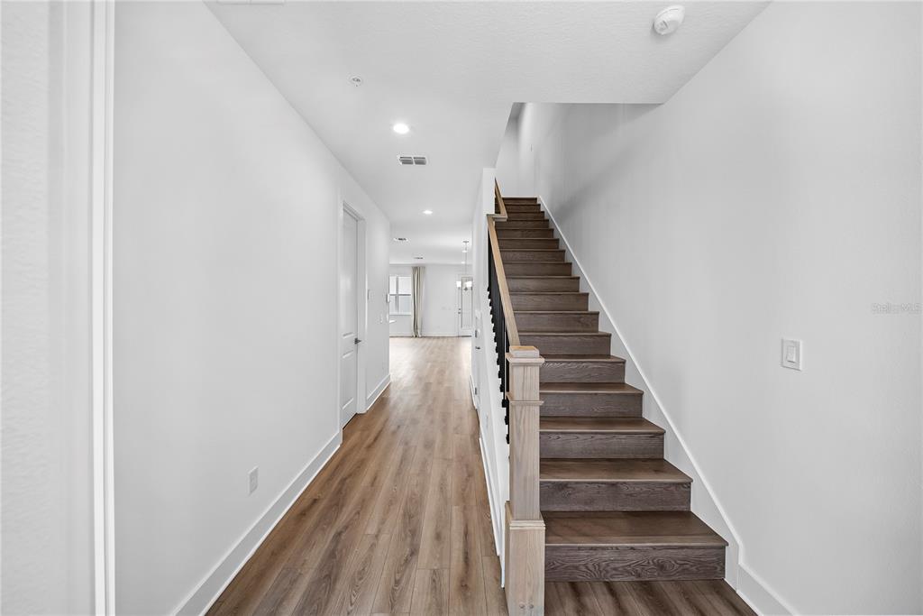 A hallway with wood-look flooring leads to an open living area beside a wooden staircase — 1856 CROWNCREST DRIVE, APOPKA, FL