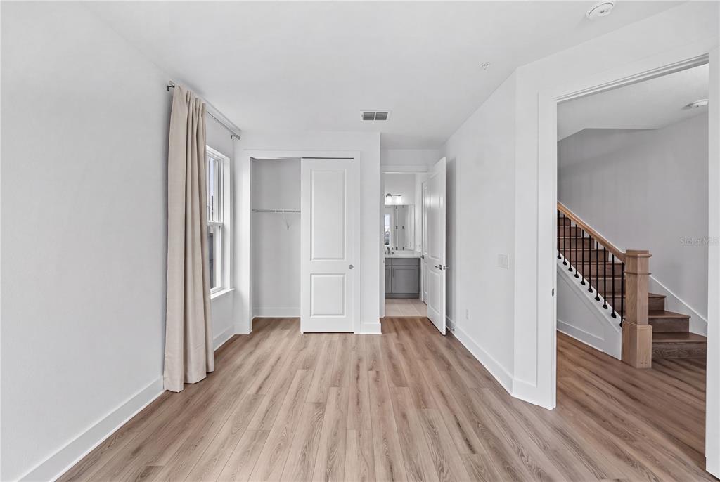 A bedroom with light wood-look flooring, a closet, and an open doorway to a staircase — 1856 CROWNCREST DRIVE, APOPKA, FL