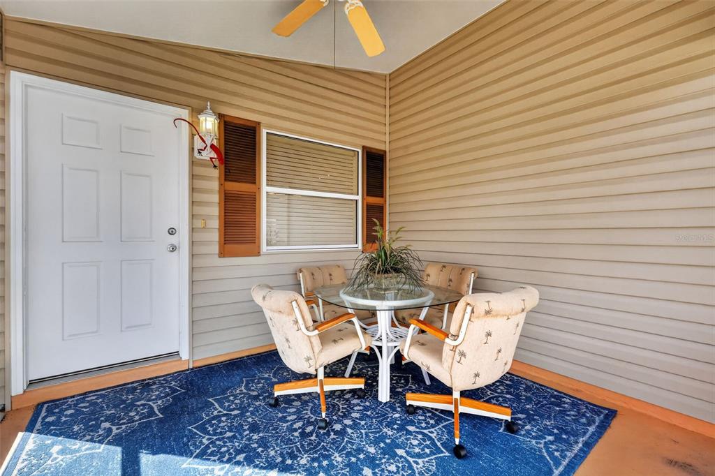 A covered patio features a glass-top table, four chairs, and a blue patterned rug — 2581 ERROL TERRACE, THE VILLAGES, FL