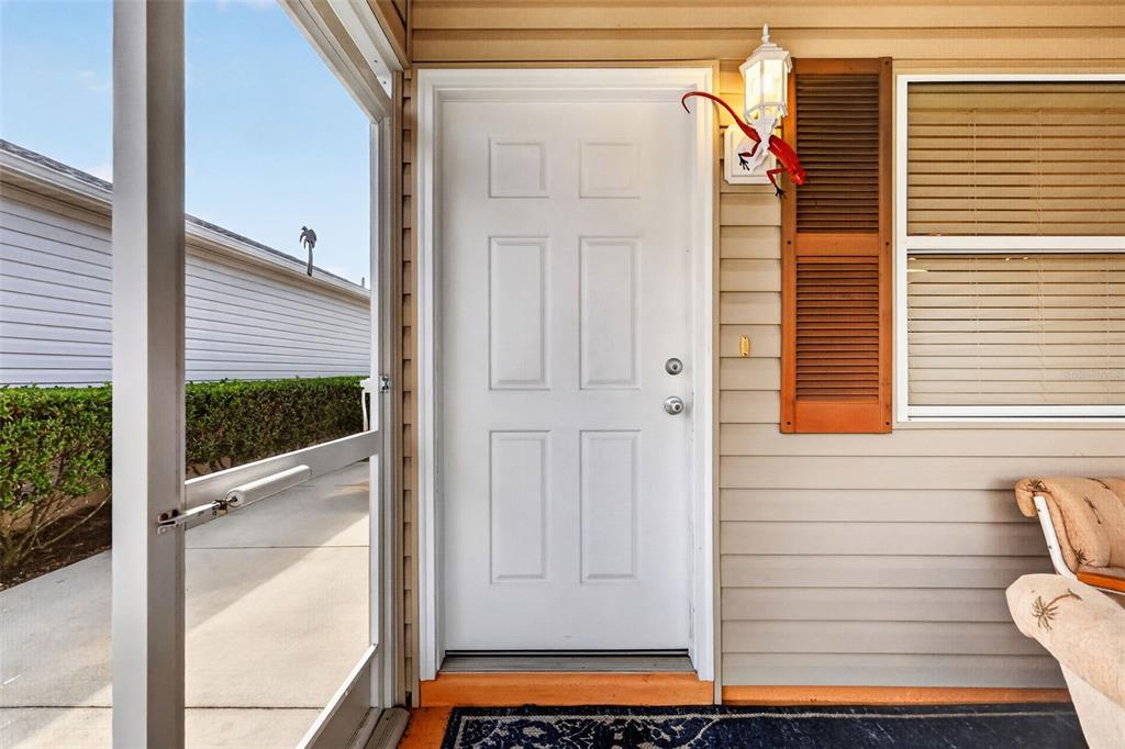 A white six-panel door is centered on a covered porch with beige siding and shutters — 2581 ERROL TERRACE, THE VILLAGES, FL