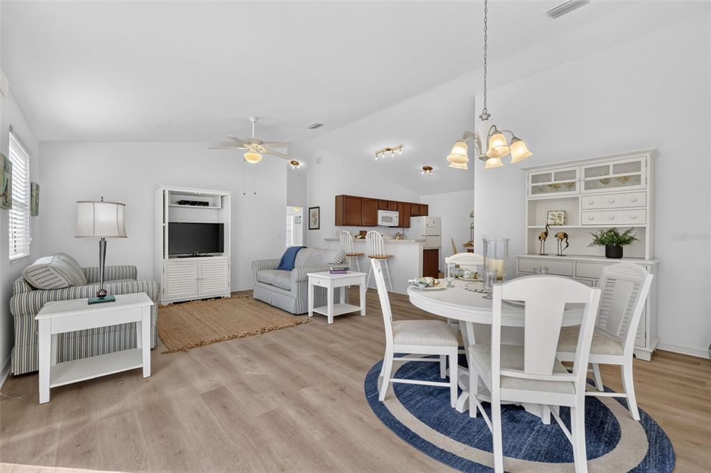 An open-concept living and dining area features light wood flooring, white furniture, and a kitchen — 2581 ERROL TERRACE, THE VILLAGES, FL