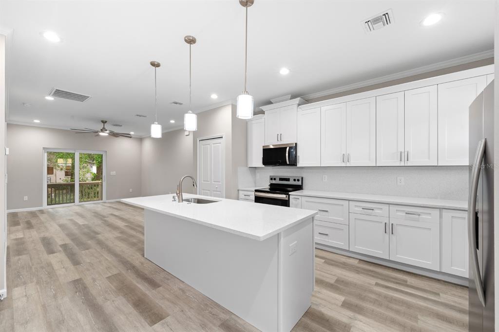 A modern kitchen with white cabinets, a central island, and light wood-look flooring — 2915 CHIPCO STREET, TAMPA, FL