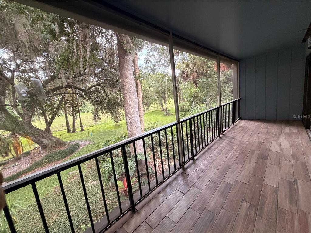 A screened-in balcony features wood-look tile flooring, a black metal railing, and a view of trees — 423 SHEOAH BOULEVARD UNIT 14, WINTER SPRINGS, FL