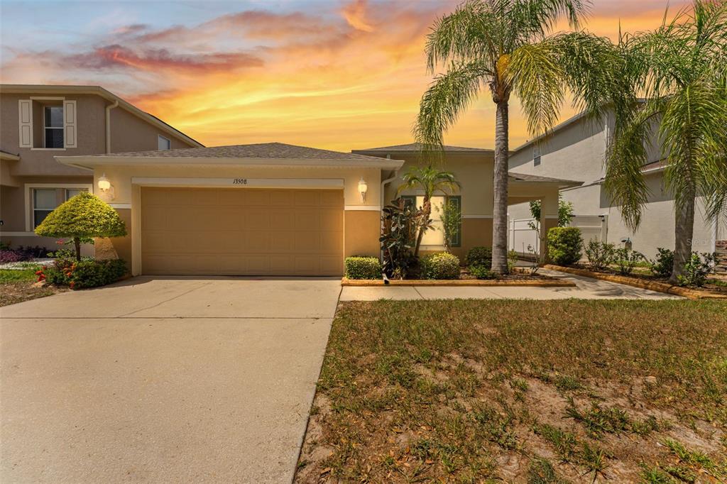 A single-story house with a two-car garage, a palm tree, and a sunset sky — 13508 RED EAR COURT, RIVERVIEW, FL