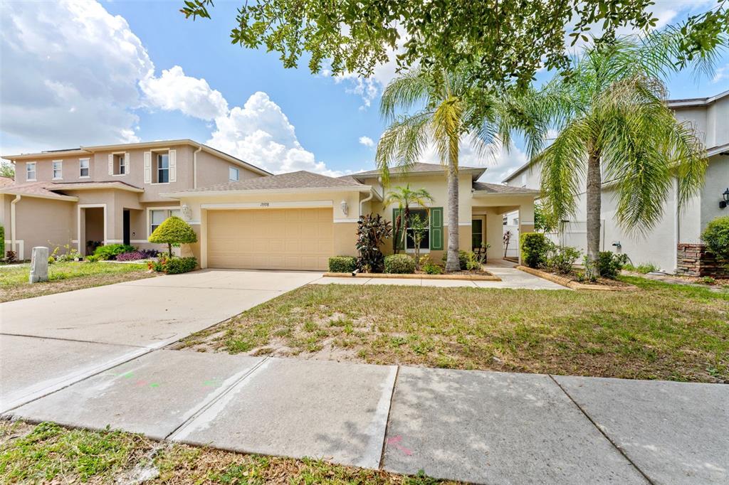 A single-story suburban house with a tan stucco exterior, two-car garage, and two palm trees — 13508 RED EAR COURT, RIVERVIEW, FL