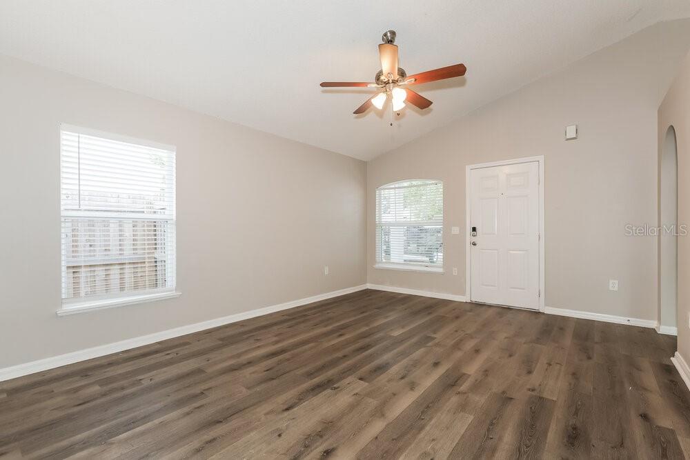 An empty living room features light-colored walls, wood-look flooring, a ceiling fan, and two windows — 30319 BIRDHOUSE DRIVE, WESLEY CHAPEL, FL