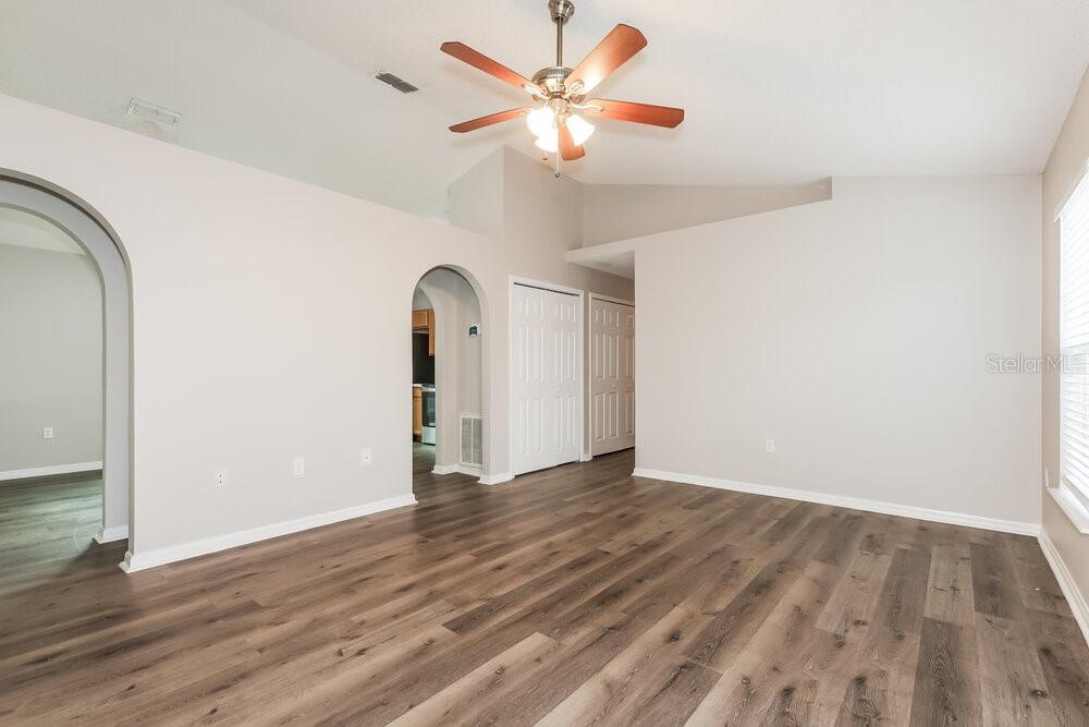 An empty room features light-colored walls, wood-look flooring, a ceiling fan, and arched doorways — 30319 BIRDHOUSE DRIVE, WESLEY CHAPEL, FL