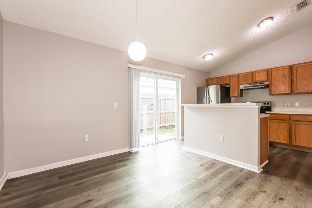 A dining area with wood-look flooring, a pendant light, and an adjacent kitchen with cabinets — 30319 BIRDHOUSE DRIVE, WESLEY CHAPEL, FL
