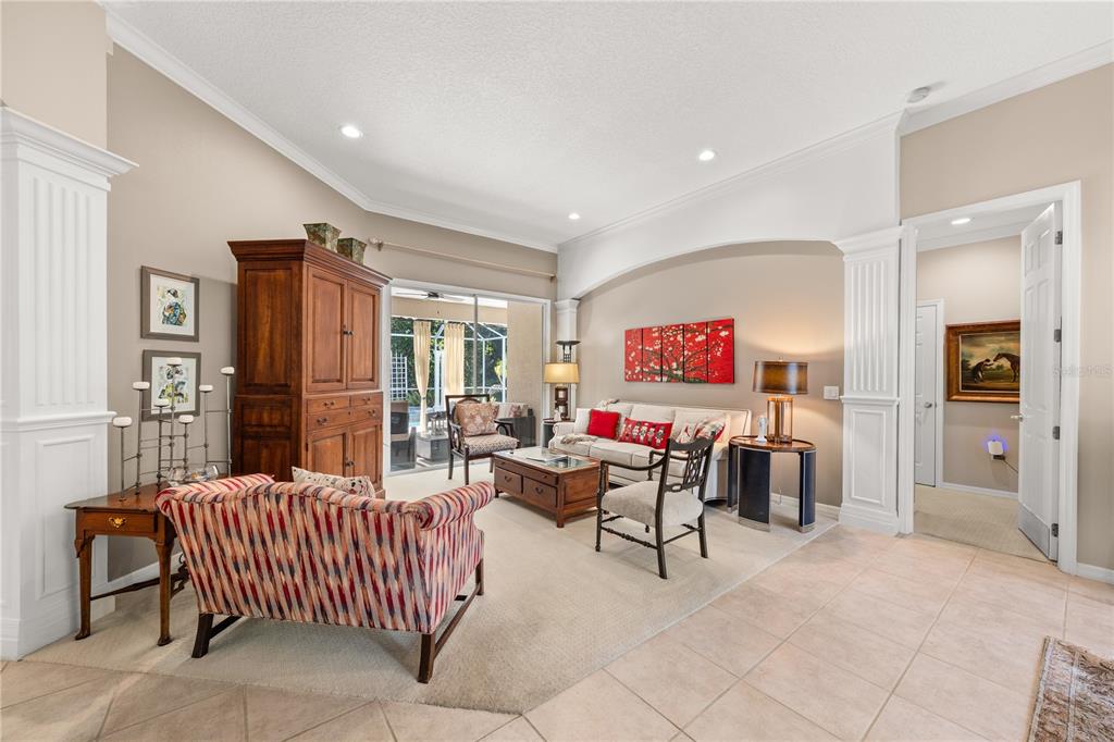 A living room features a beige sofa, patterned armchair, wooden cabinet, and tile flooring — 8224 WATERVIEW BOULEVARD, LAKEWOOD RANCH, FL