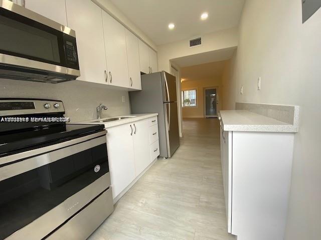 A galley kitchen features white cabinets, stainless steel appliances, and light-colored flooring — 3530 SW 9th Ter # 6B, Miami FL 33135, MIAMI, FL