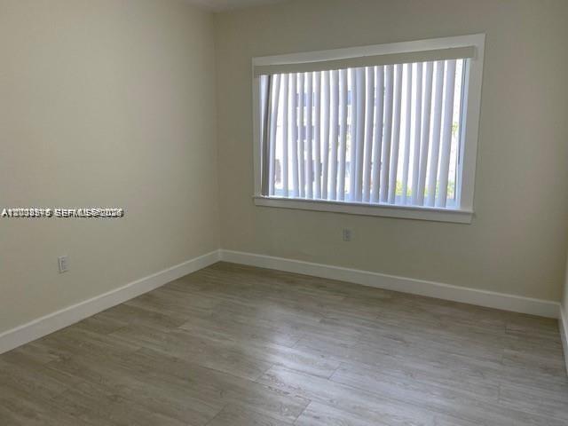An empty room features light-colored wood-look flooring, beige walls, and a window with vertical blinds — 3530 SW 9th Ter # 6B, Miami FL 33135, MIAMI, FL