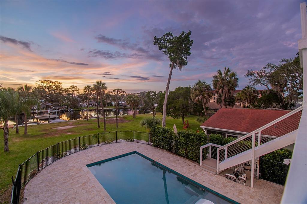 An elevated view of a backyard swimming pool, lawn, and canal at sunset — 6121 LAFAYETTE STREET, NEW PORT RICHEY, FL