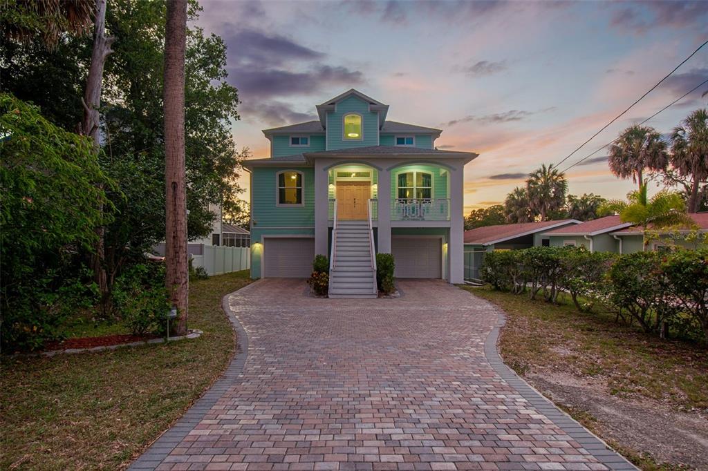 A three-story, light green elevated house with a brick paver driveway and two garage bays — 6121 LAFAYETTE STREET, NEW PORT RICHEY, FL