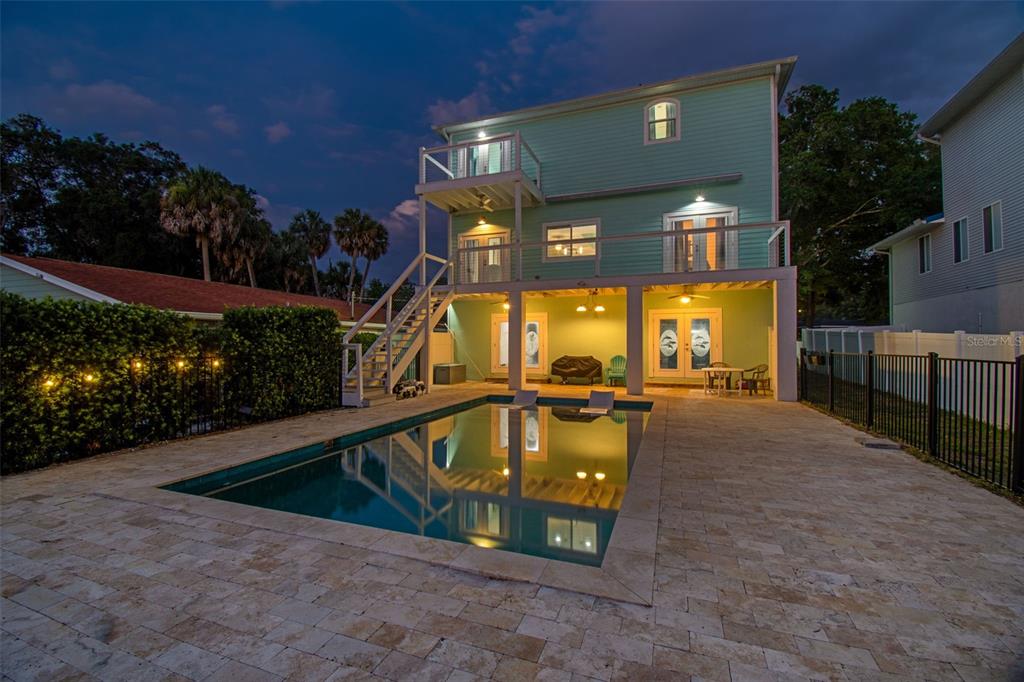 A three-story light green house with a swimming pool and a stone patio at dusk — 6121 LAFAYETTE STREET, NEW PORT RICHEY, FL