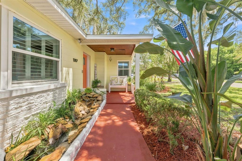 A red walkway leads to a covered porch with a bench and a stone water feature — 1317 DIVOT LANE, TAMPA, FL