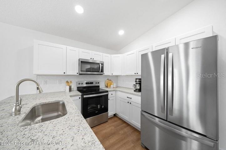 A kitchen features white cabinets, stainless steel appliances, and a granite-topped island with a sink — 12470 BARNEVELDE ROAD, WEEKI WACHEE, FL