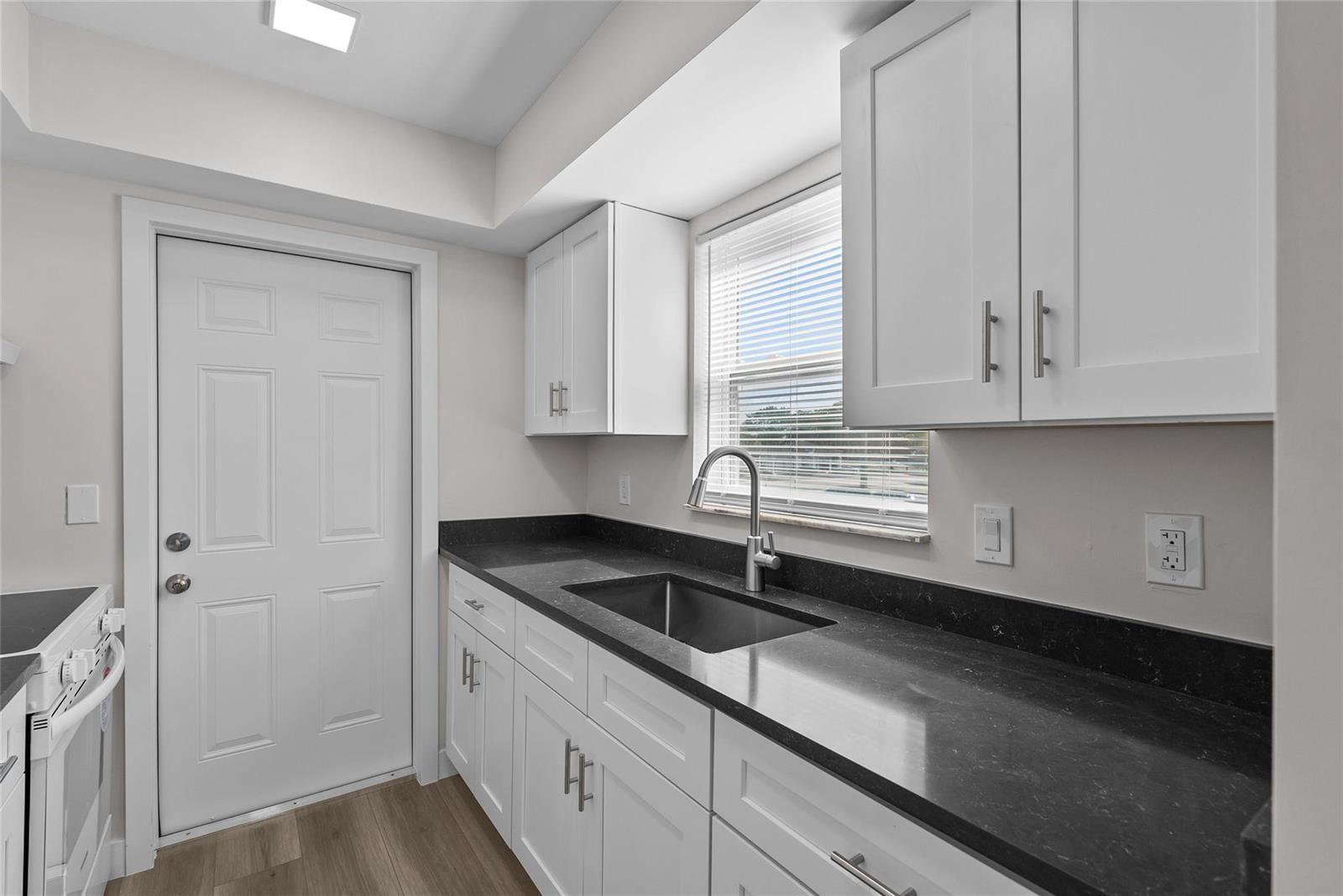 A kitchen features white cabinets, dark countertops, a stainless steel sink, and a white door — 1150 E Sample Road # 202, Pompano Beach FL 33064, POMPANO BEACH, FL