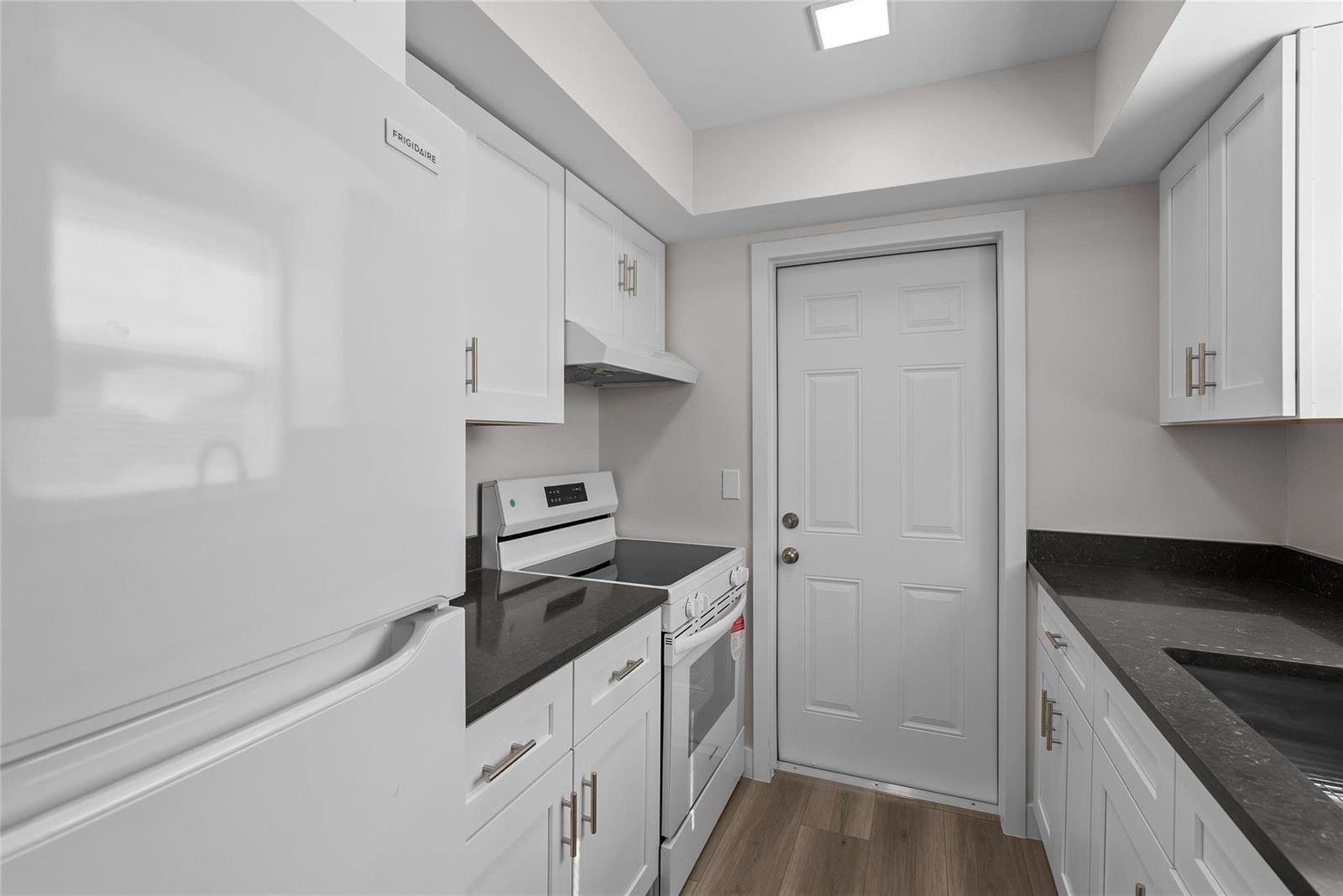 A galley kitchen features white cabinets, dark countertops, and white appliances — 1150 E Sample Road # 202, Pompano Beach FL 33064, POMPANO BEACH, FL