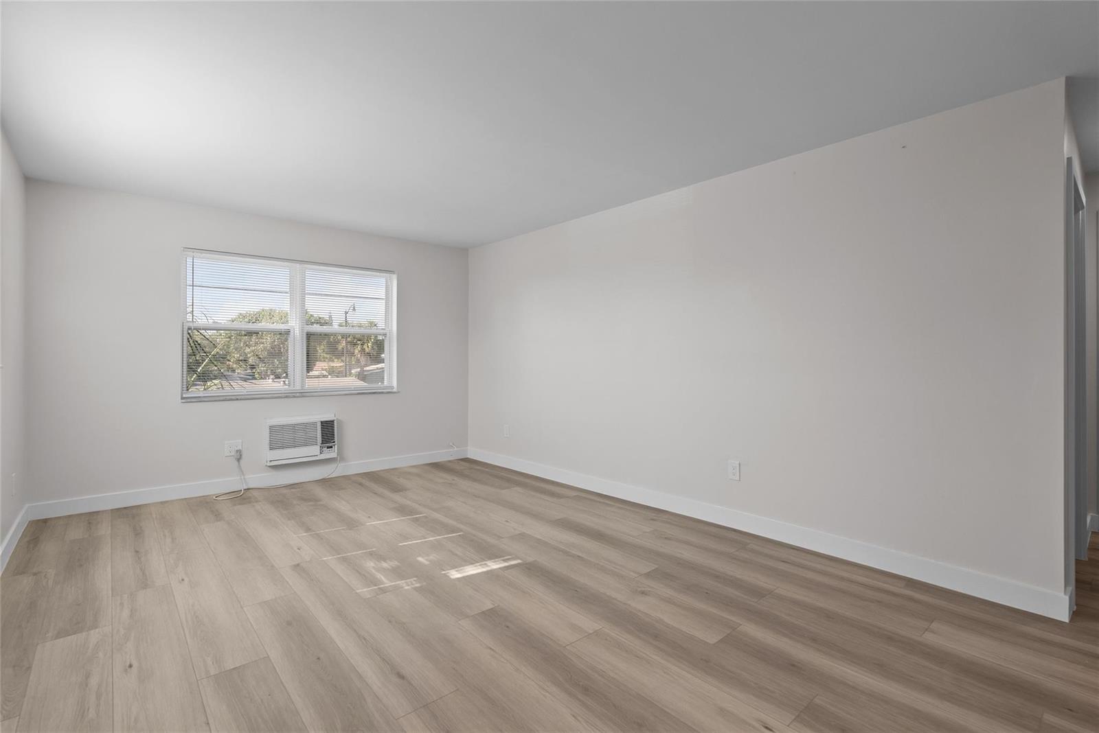An empty bedroom features light wood-look flooring, white walls, and a window air conditioning unit — 1150 E Sample Road # 202, Pompano Beach FL 33064, POMPANO BEACH, FL