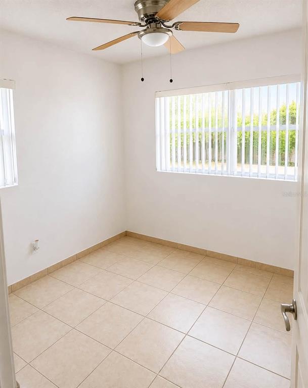 An empty room features white walls, light-colored tile flooring, a ceiling fan, and vertical blinds — 208 PALMYRA DRIVE, ORLANDO, FL