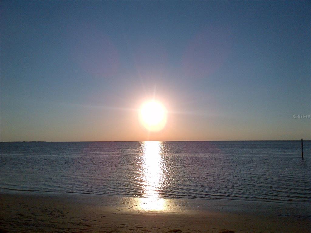 A bright sun sets over the ocean, casting a reflection on the sandy beach — 21 WESTSHORE DRIVE, NEW PORT RICHEY, FL
