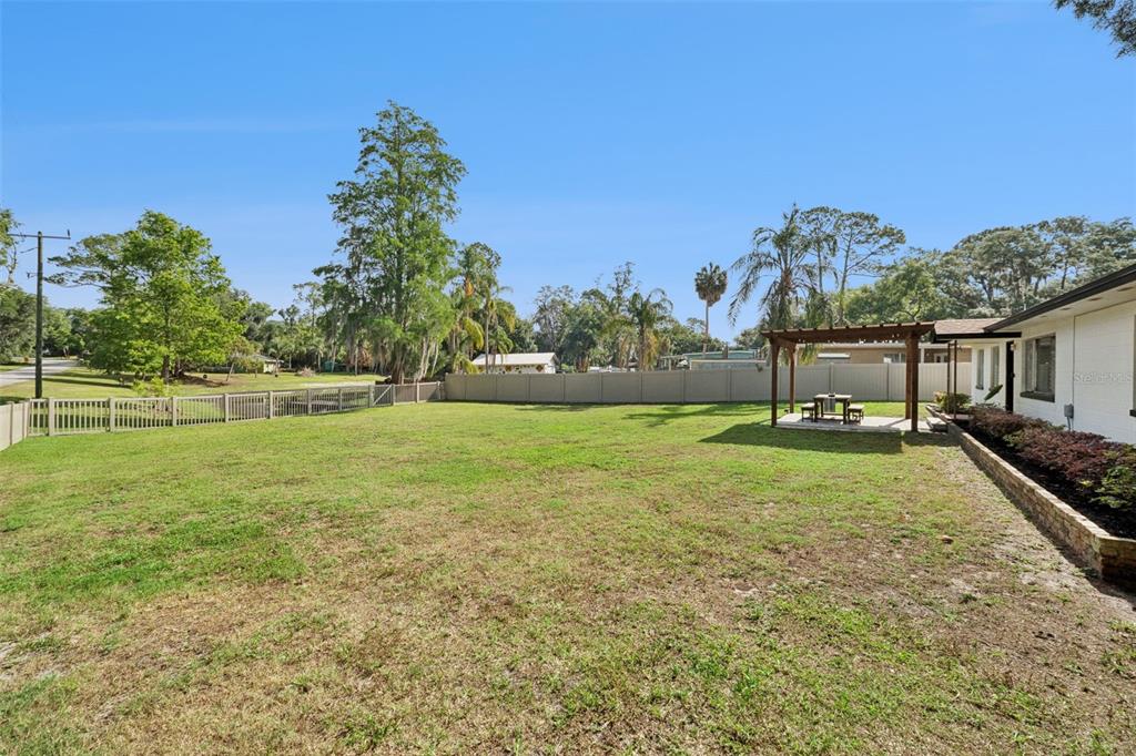 A grassy backyard features a wooden pergola, a patio table, and a vinyl privacy fence — 219 S CRYSTAL DRIVE, SANFORD, FL