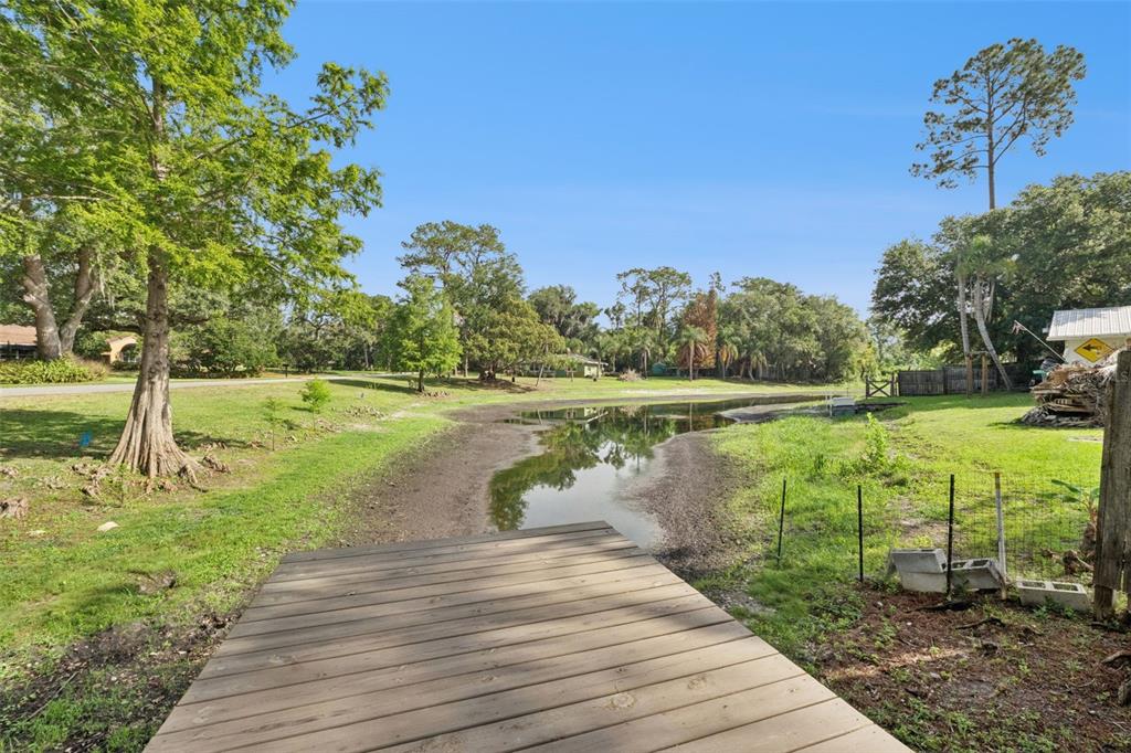 A wooden dock overlooks a narrow, partially dried-up pond surrounded by trees and grass — 219 S CRYSTAL DRIVE, SANFORD, FL