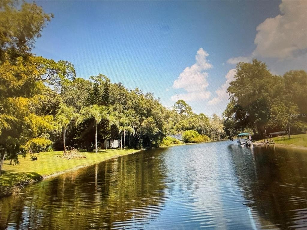 A view of a narrow canal lined with trees, grass, and a small boat — 219 S CRYSTAL DRIVE, SANFORD, FL