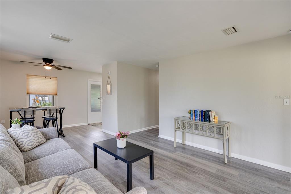 A living room features gray wood-look flooring, a gray sofa, and a glass-topped console table — 3213 NORMANDY DRIVE E, PORT CHARLOTTE, FL
