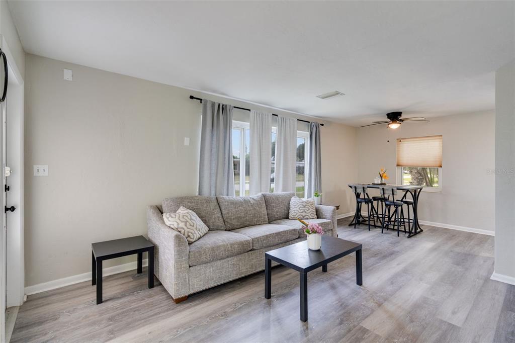 A living room with light gray flooring, a gray sofa, and a small dining table — 3213 NORMANDY DRIVE E, PORT CHARLOTTE, FL