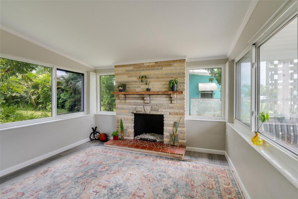A sunroom features a stone fireplace, a tiled hearth, and large windows overlooking the yard — 3213 NORMANDY DRIVE E, PORT CHARLOTTE, FL