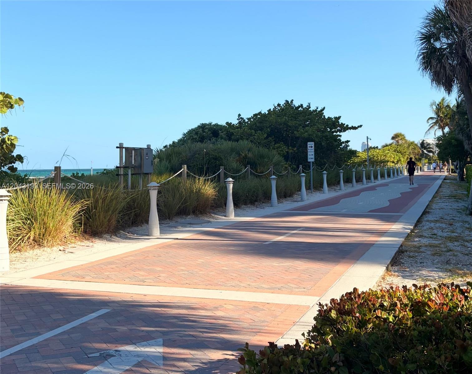 A paved walkway with bollards runs alongside coastal vegetation and the ocean — 2625 Collins Ave # 215, Miami Beach FL 33140, MIAMI BEACH, FL