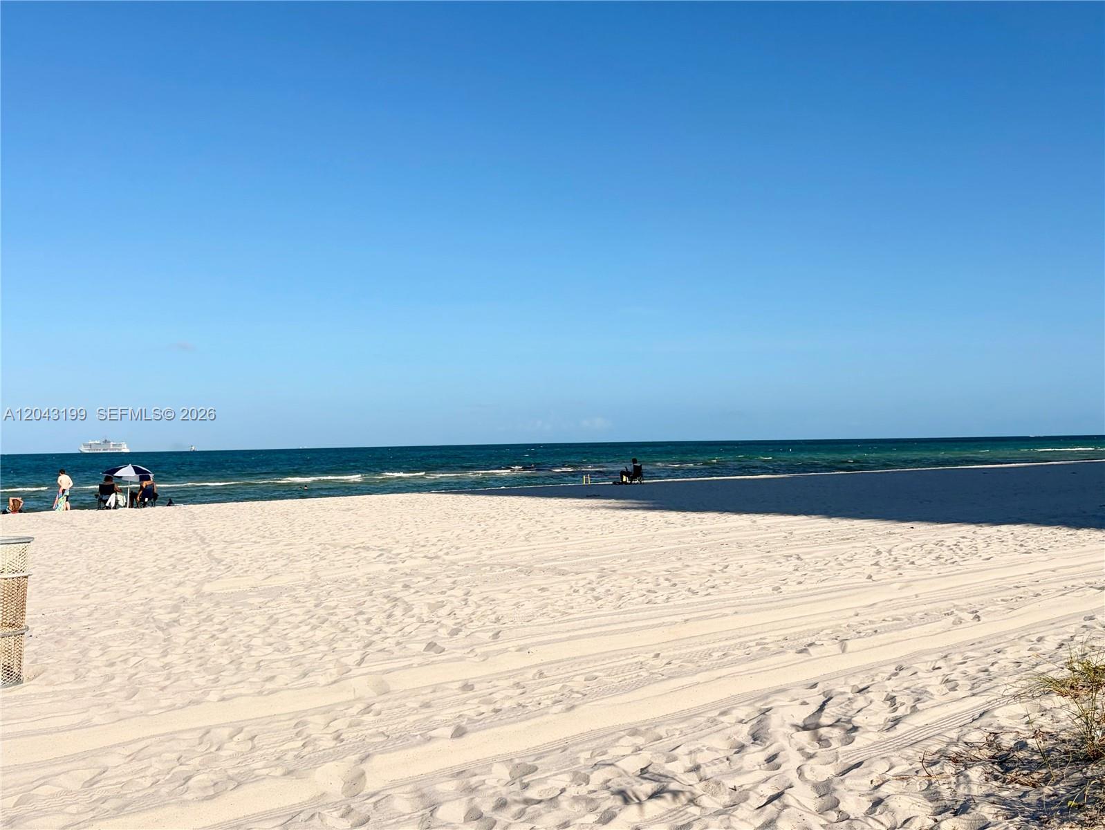 A wide, sandy beach stretches toward the ocean under a clear blue sky — 2625 Collins Ave # 215, Miami Beach FL 33140, MIAMI BEACH, FL