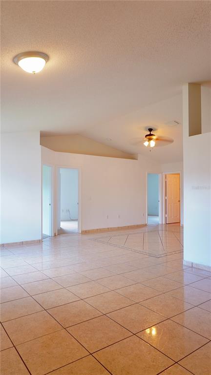 A bright, open-concept room features light-colored tile flooring, a vaulted ceiling, and multiple doorways — 1011 CANNES DRIVE, KISSIMMEE, FL