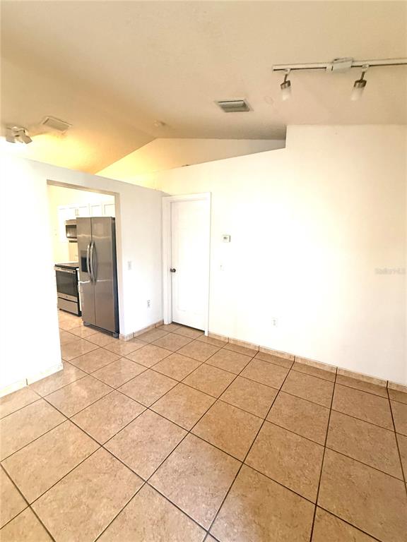 A room with tan tile flooring, white walls, a vaulted ceiling, and a doorway to a kitchen — 1011 CANNES DRIVE, KISSIMMEE, FL